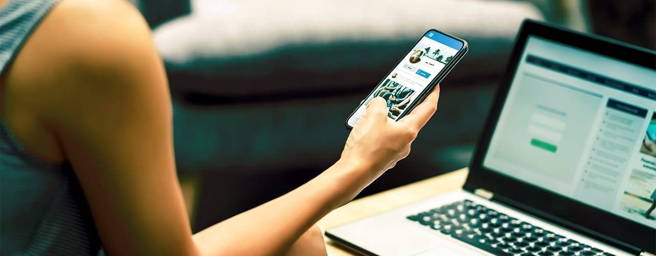Photo of a person holding a mobile phone in front of a laptop